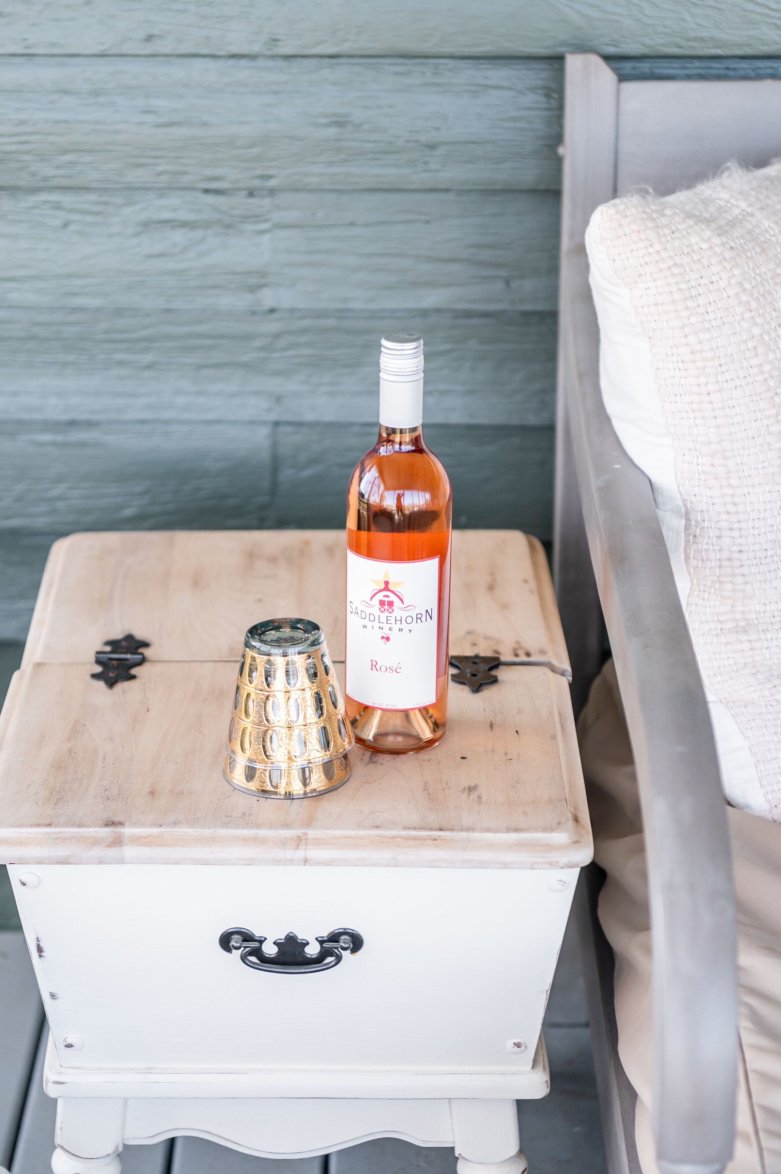 A white chest of drawers with a bottle of wine and a glass on top.