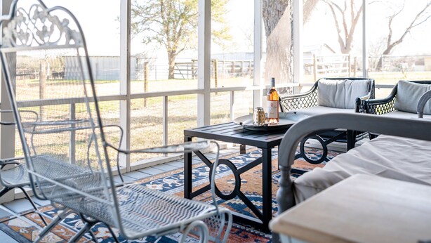 Un patio couvert avec des chaises et une table en métal, sur laquelle on peut voir une bouteille et des verres.