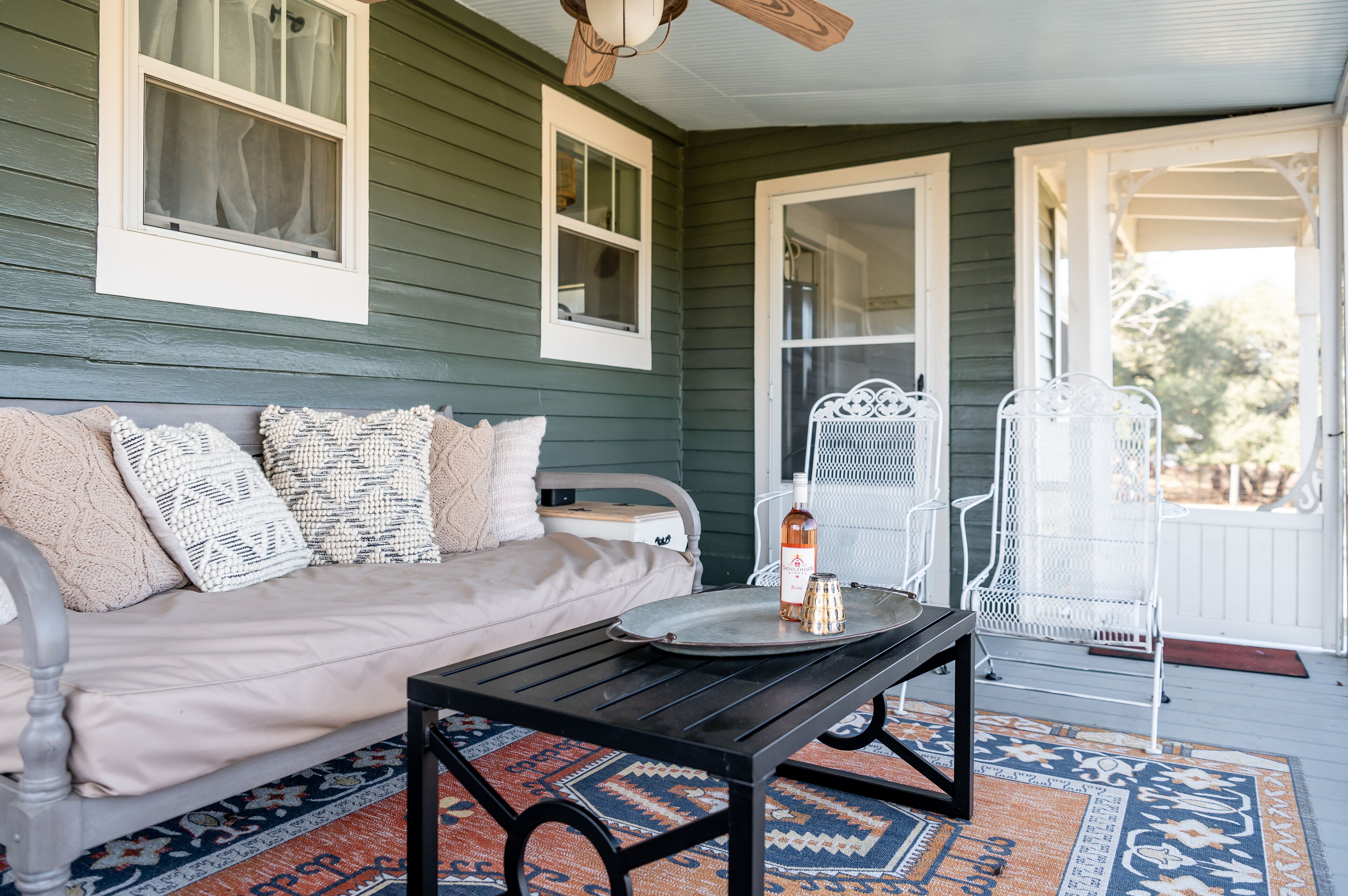 A cozy porch with a sofa, a metal table, and white chairs.