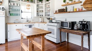 Une cuisine avec des meubles blancs, des plans de travail en bois, une table en bois, une cuisinière, un four à micro-ondes et une machine à café.