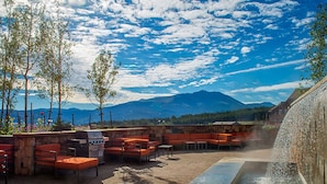 Eine Terrasse im Freien mit Sitzgelegenheiten und einem Wasserspiel, mit Blick auf eine gebirgige Landschaft.