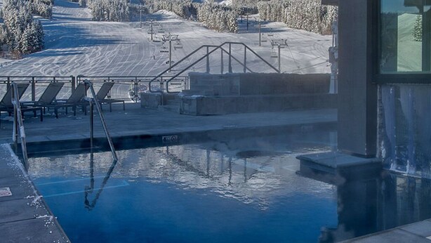 Ein Poolbereich mit Blick auf einen verschneiten Berg und Skipisten.