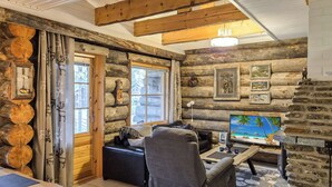 A cozy log cabin interior with a fireplace, a comfortable seating area, and a large window offering a view of the outside.