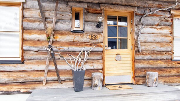 A log cabin with a wooden door, a small window, and a number 'B8' on the wall.