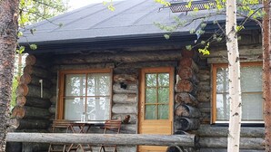 A log cabin with a porch, two windows, and a bench.