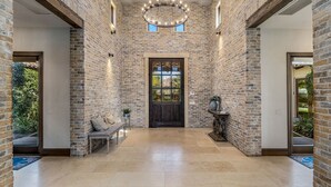 A spacious foyer with exposed brick walls, a central door with glass panels, and a bench with cushions. - Private Estate - Enough amenities to keep kids and adults having a great time (Bermuda Dunes)