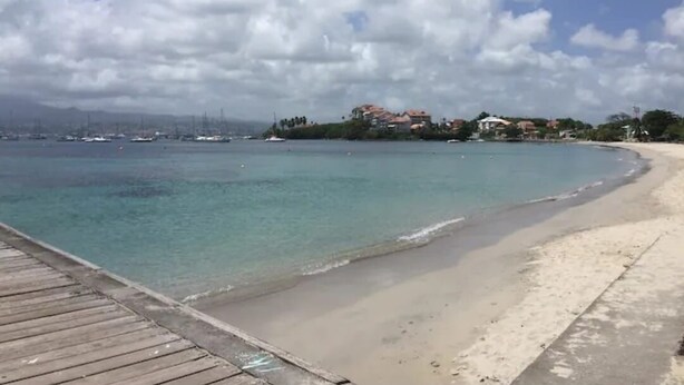 A beach with a wooden pier extending into calm waters, a clear sky, and buildings in the background. - Studio Vacances Martinique 3 ilets (Trois ilets)