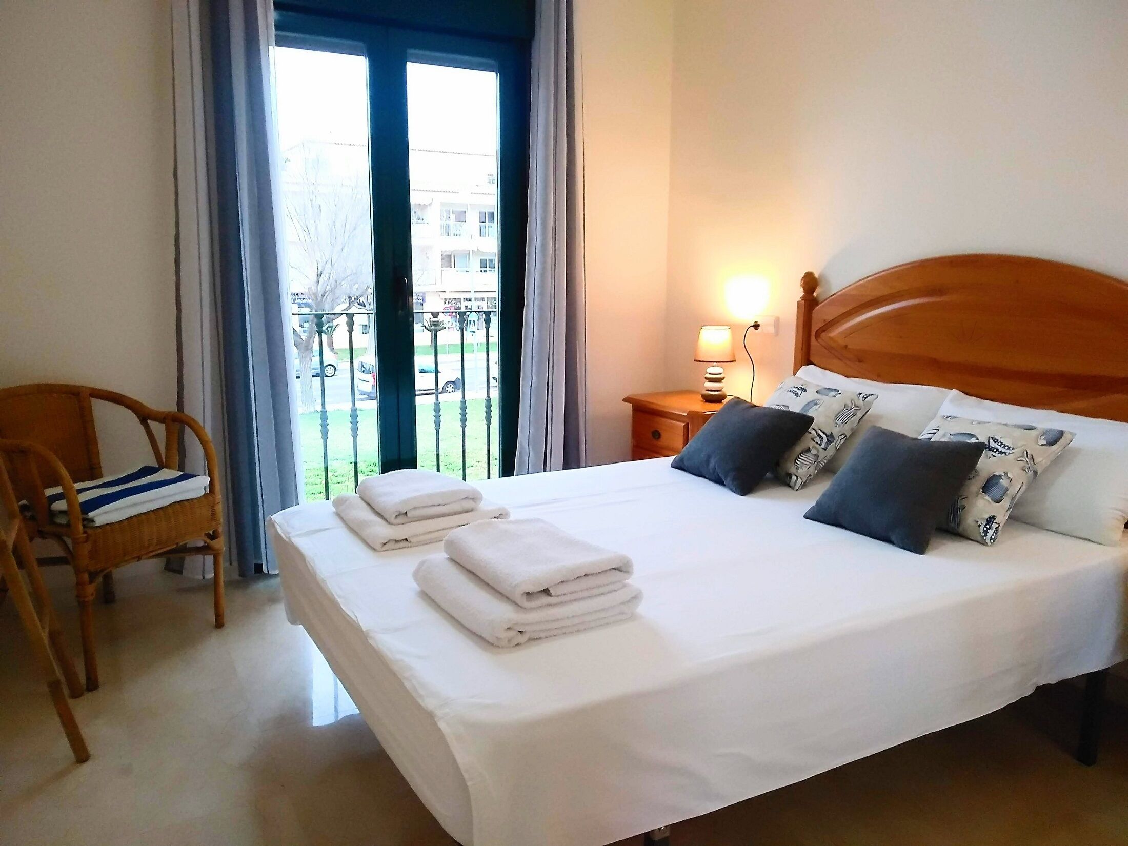 A neatly made bed with white linens and folded towels, a wooden headboard, and a nightstand with a lamp.