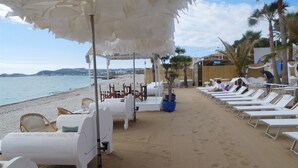 Een strandlounge met witte ligbedden en een overdekte zithoek.