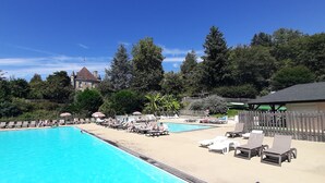 A swimming pool area with lounge chairs and umbrellas, surrounded by trees and a building in the background.