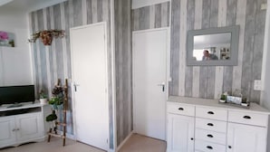 A room with a TV on a white cabinet, a wooden ladder, and a white wardrobe with a mirror above it.