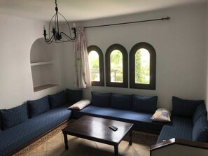 A room with a dark wooden coffee table, a blue sofa with patterned cushions, and three arched windows providing natural light.