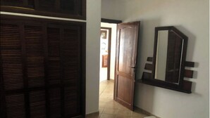 Una habitación con una cama, una puerta de madera, un espejo y suelo de baldosas.