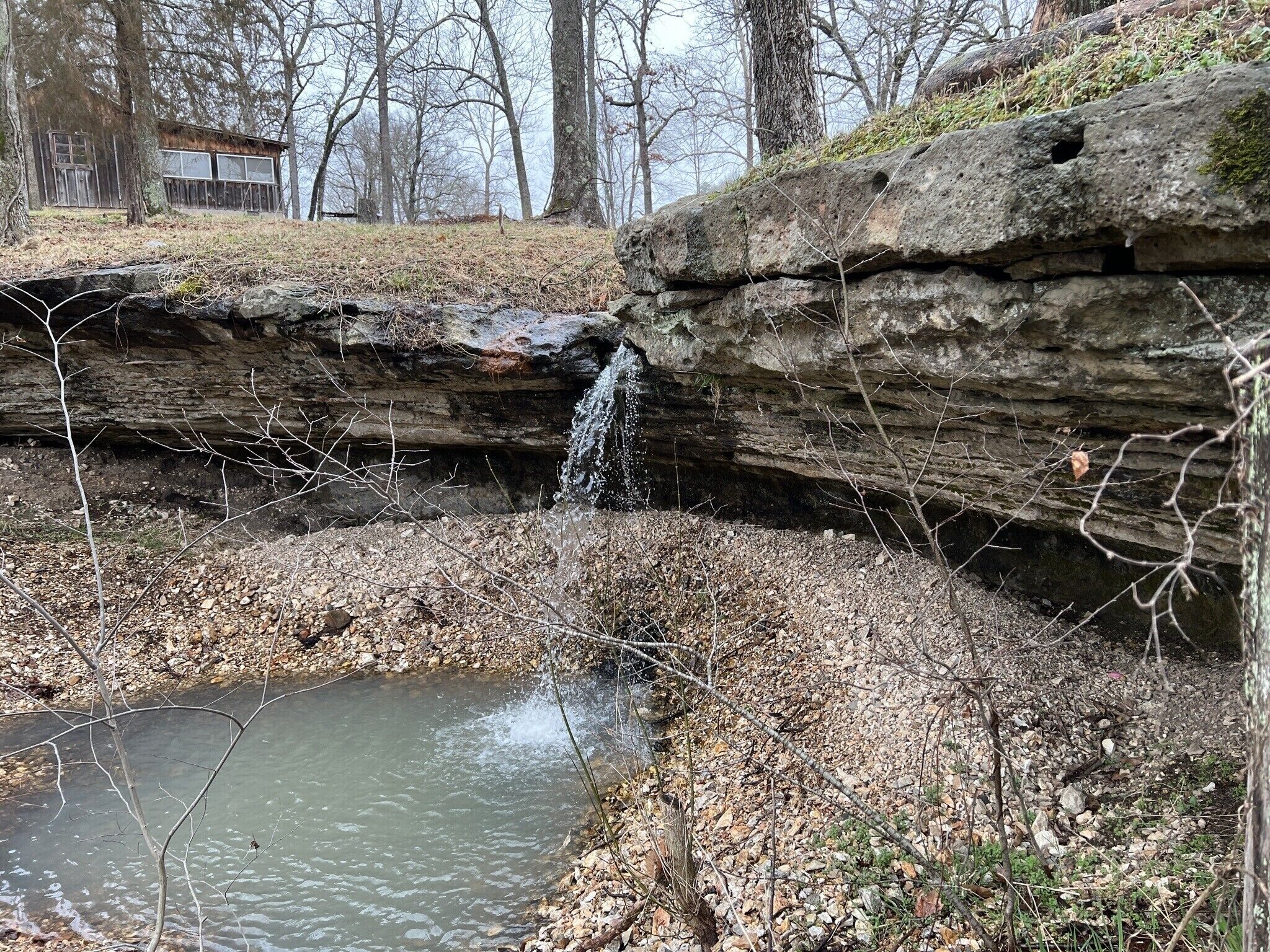 A natural landscape with a waterfall, rocky terrain, and a small pond.