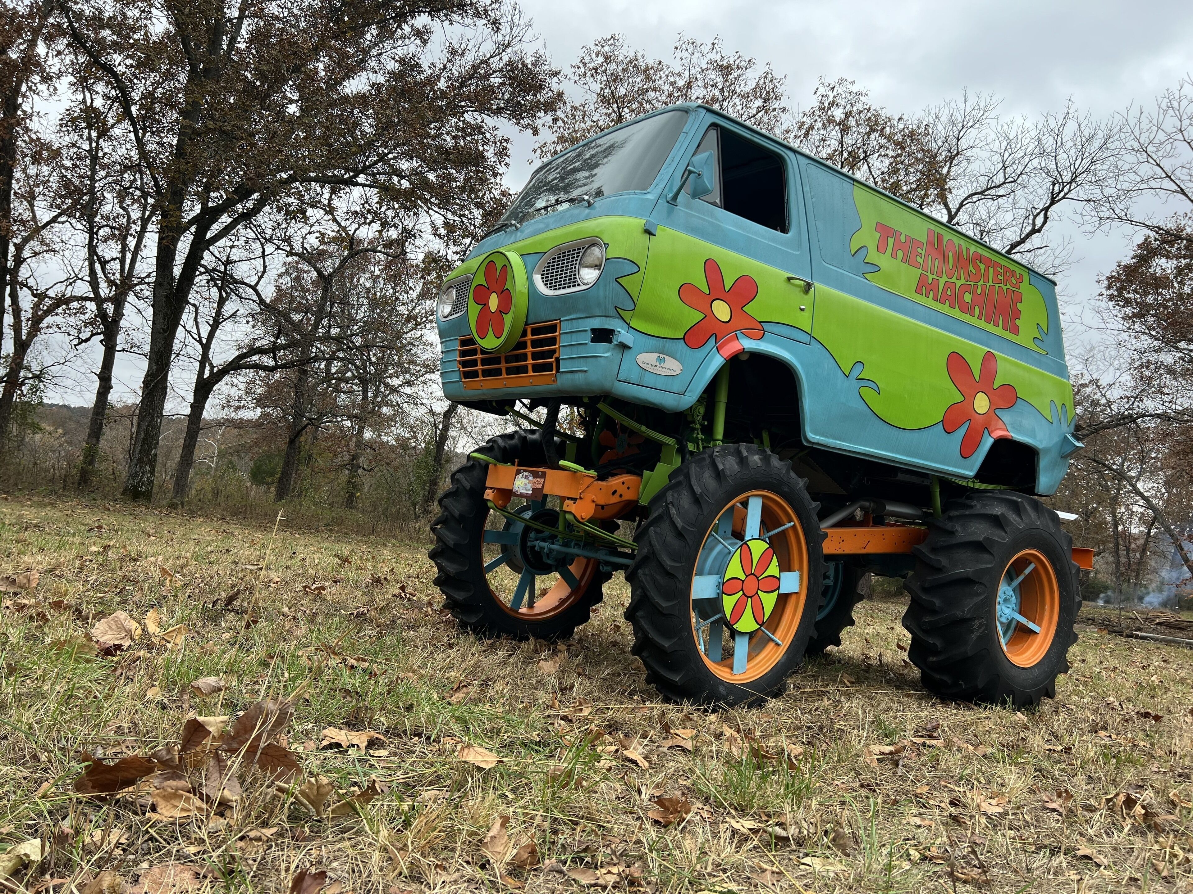 A large, colorful truck with the text "THE MONSTER MACHINE" on its side, parked in a grassy area with trees in the background.