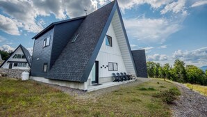 Une maison moderne avec un toit en pente, un petit porche avec des chaises et un ciel dégagé.
