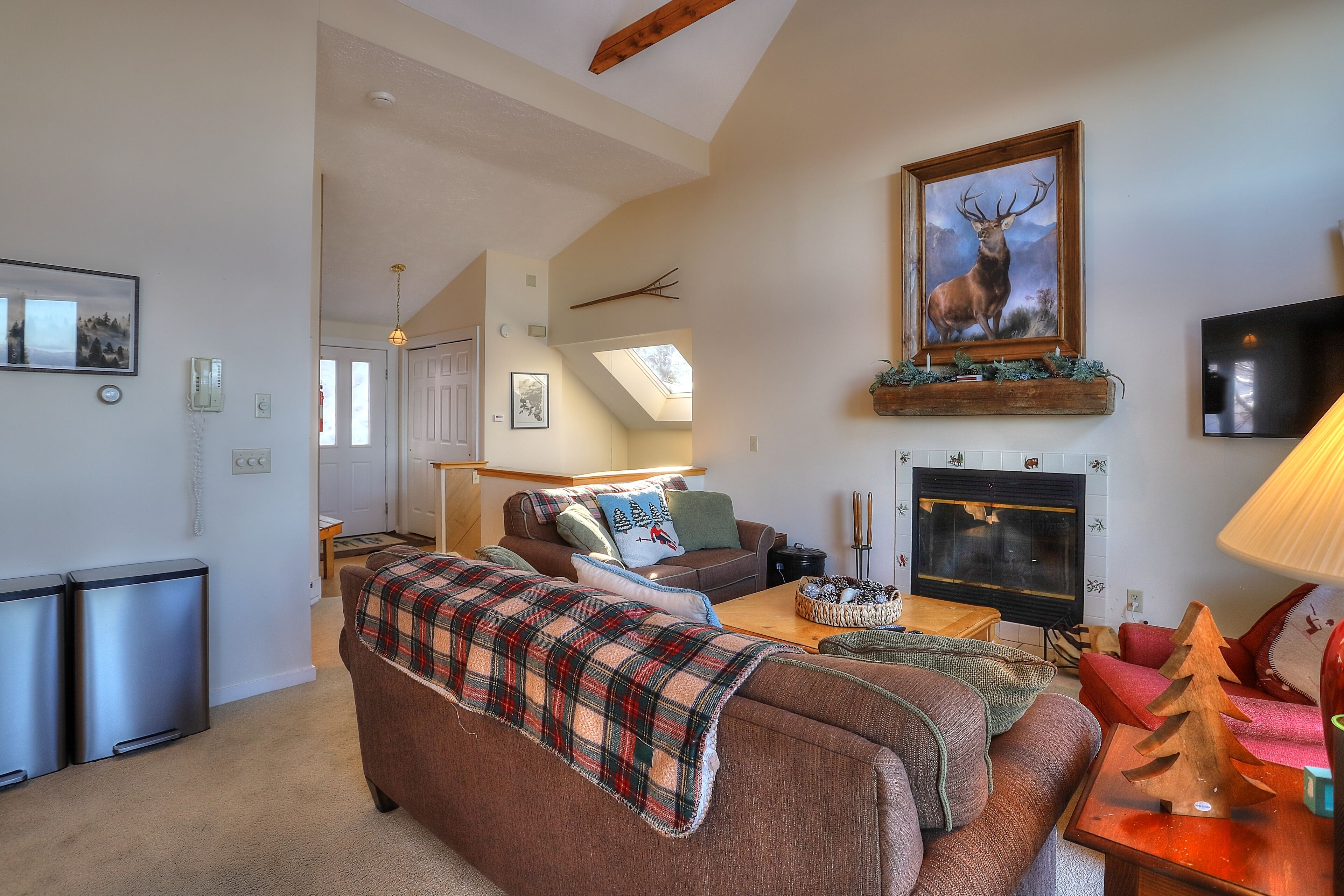 A cozy living room with a fireplace, a sofa with a plaid blanket, and a mounted deer painting.