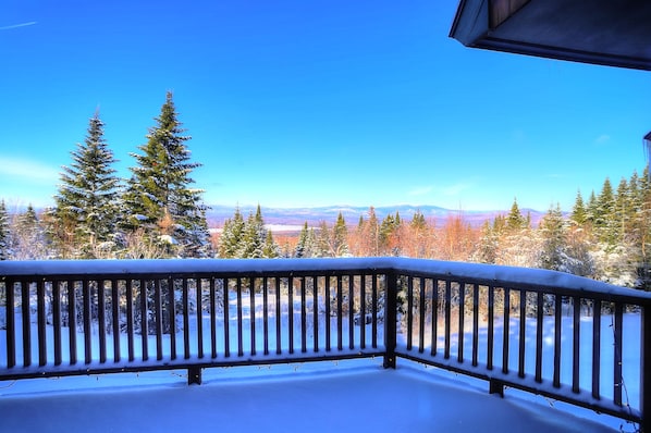 Ein mit Schnee bedeckter Balkon mit Blick auf immergrüne Bäume und ferne Berge.