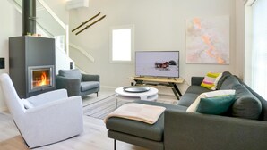 Ein modernes Wohnzimmer mit Kamin, grauen Sofas, einem Fernseher und einer Treppe.