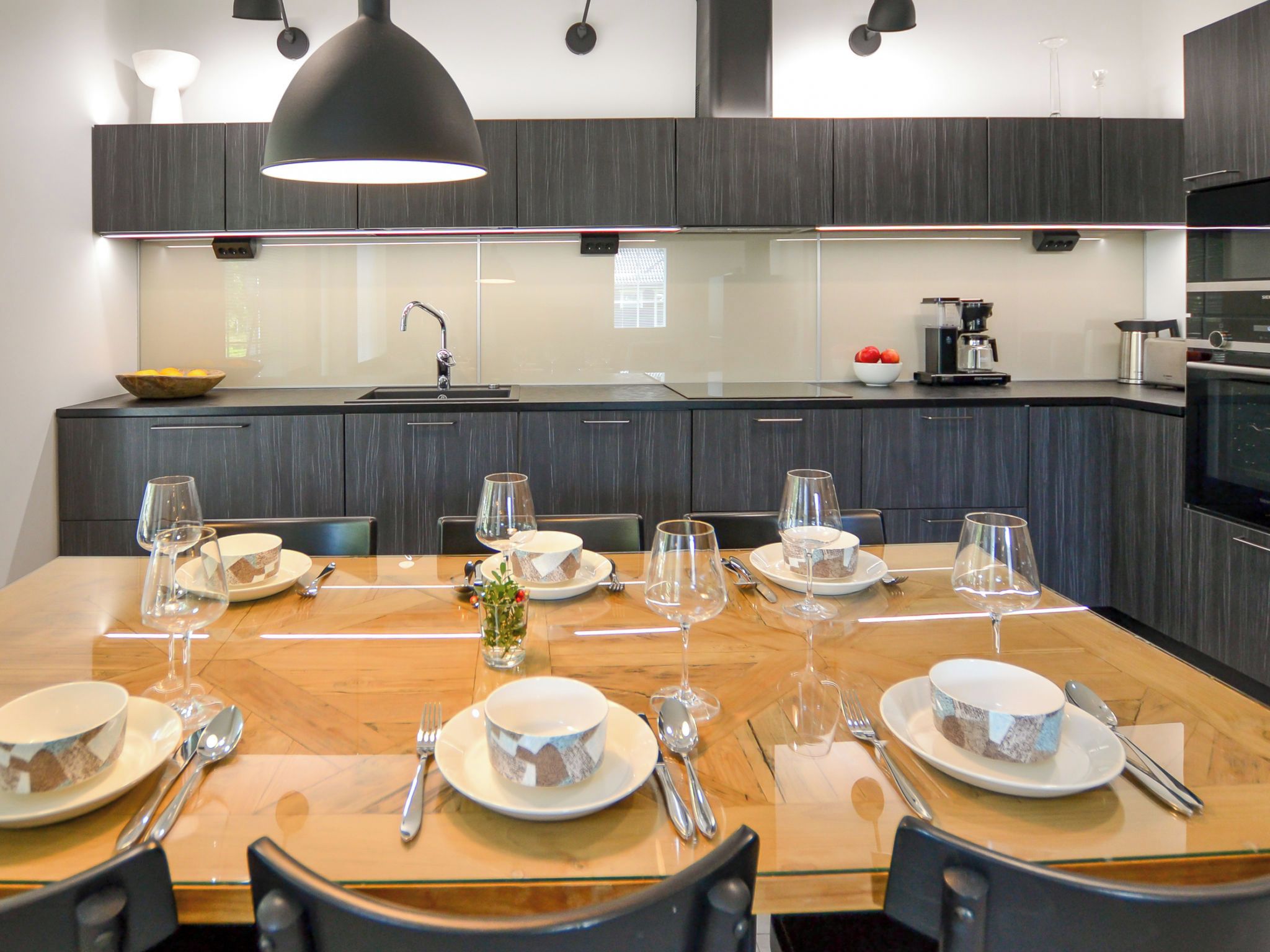 A modern kitchen with dark wood cabinets, a large island with a sink, and a dining area set for a meal.