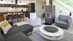 Ein modernes Wohnzimmer mit einer Couch, einem weißen Sessel und einem runden Couchtisch. Im Hintergrund ist ein Kamin zu sehen.