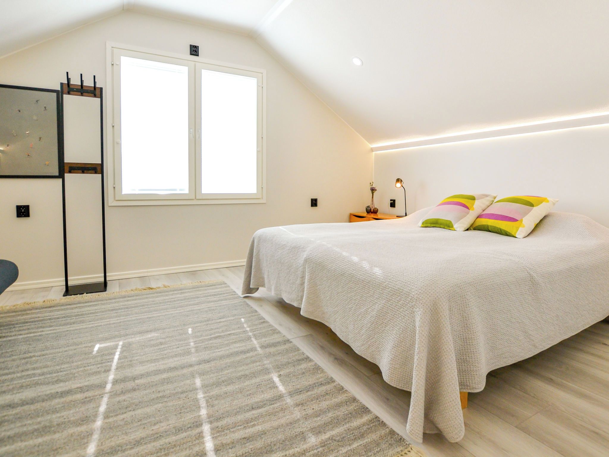 Une chambre à coucher avec un lit, une fenêtre, une table de chevet et une lampe.