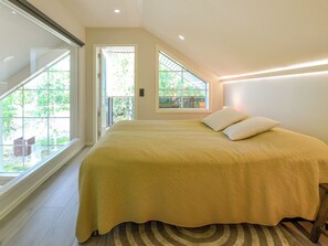 Une chambre avec un grand lit, une vue sur la verdure et un puits de lumière.