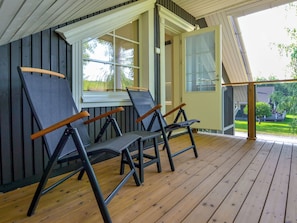 Un espacio de estar al aire libre cubierto con dos sillas y una mesa, suelo de madera y vistas al exterior.