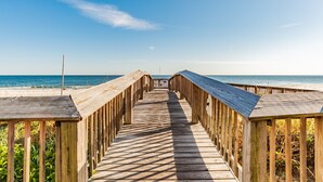 A wooden boardwalk leading to a beach with a clear sky.