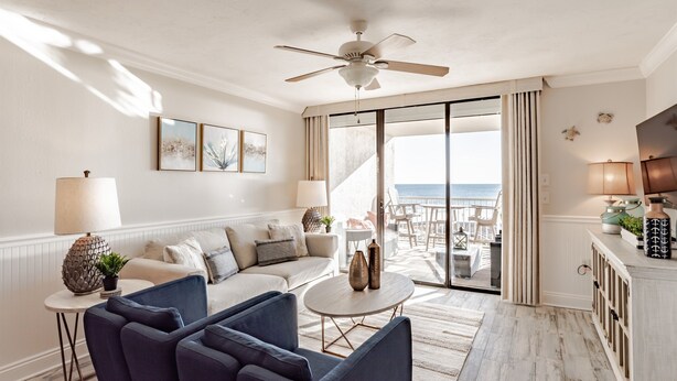 A modern living room with a sofa, chairs, a coffee table, and a view of the ocean through large sliding doors.