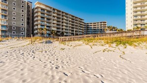 A beachfront hotel with multiple balconies, a sandy beach, and a wooden boardwalk.