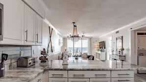 A spacious kitchen with white cabinetry, a marble countertop, and a chandelier.