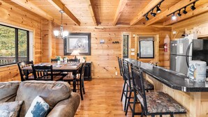 A wooden cabin interior with a dining area, kitchen, and seating space. - Experience serenity near adventure!just an 8-min drive to Top Places.  (Sevierville)