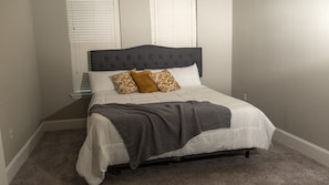 A bedroom with a bed, white bedding, a grey headboard, and patterned pillows.