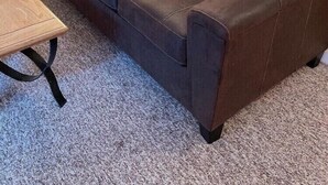 Un sofá de cuero marrón en una habitación con piso alfombrado, una lámpara y un cuadro en la pared.