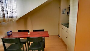 Una cocina pequeña y funcional con una mesa y sillas de madera, un armario blanco y una ventana adornada con cortinas decorativas.