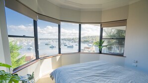 A bedroom with a large bay window overlooking a marina with boats.