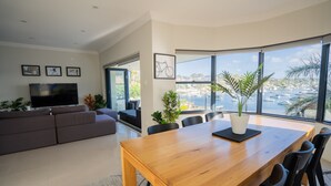 A modern living room with a large TV, a wooden dining table, and a view of a marina.