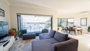 A modern living room with a large grey sofa, a flat-screen TV, and a dining area with a table and chairs.