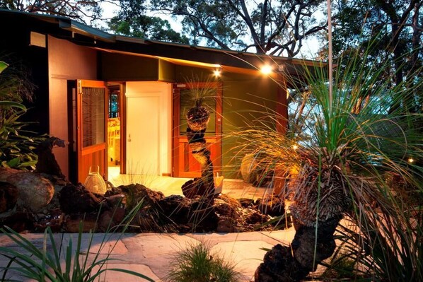 Uma casa moderna com entrada bem iluminada, rodeada por pedras e plantas.