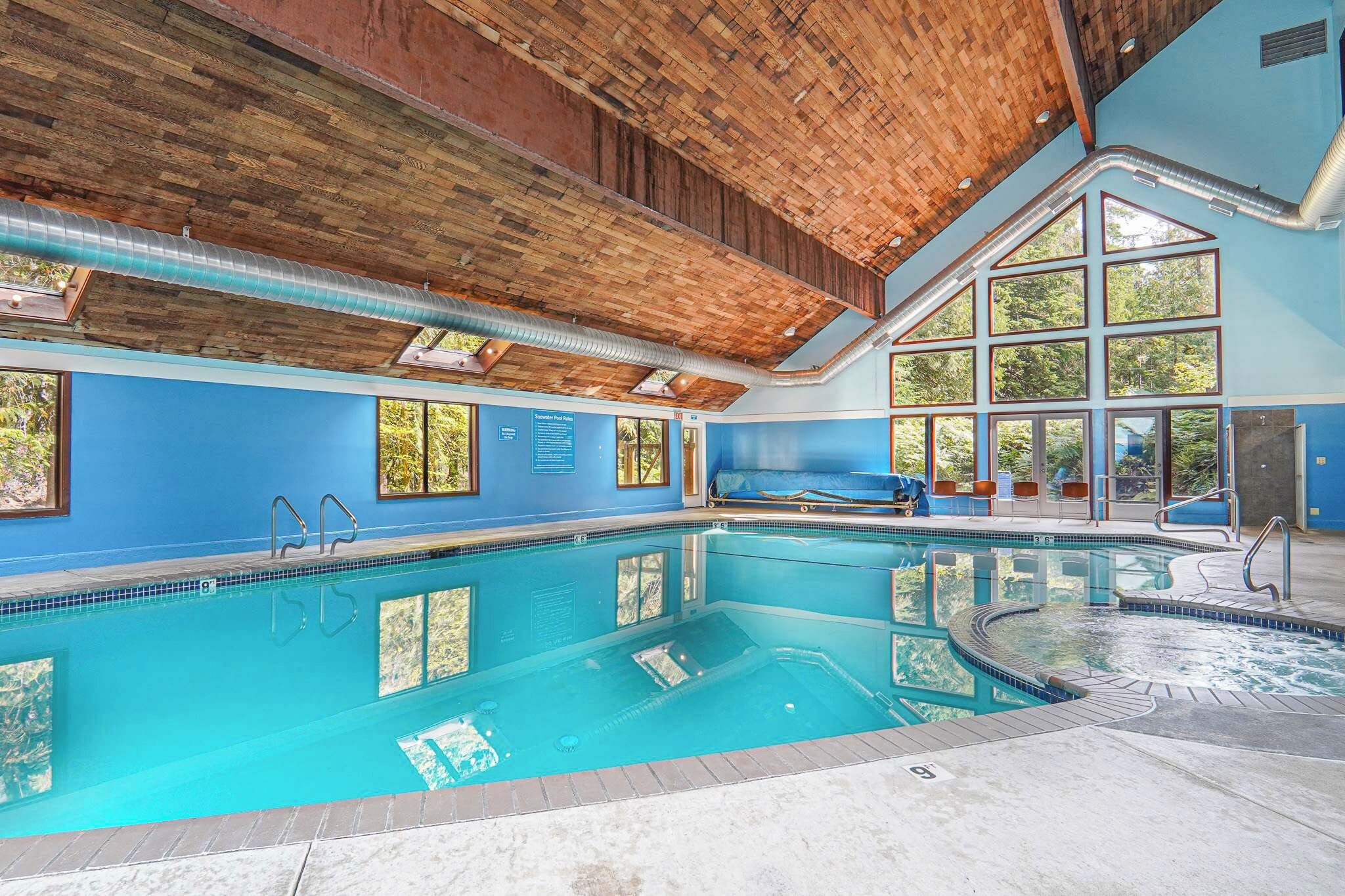 Una amplia piscina interior con techo de madera, ventanas amplias y zona de sauna.