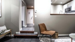 Un interior moderno con una escalera que conduce a un pasillo, una zona de estar con un banco y una cocina con microondas.