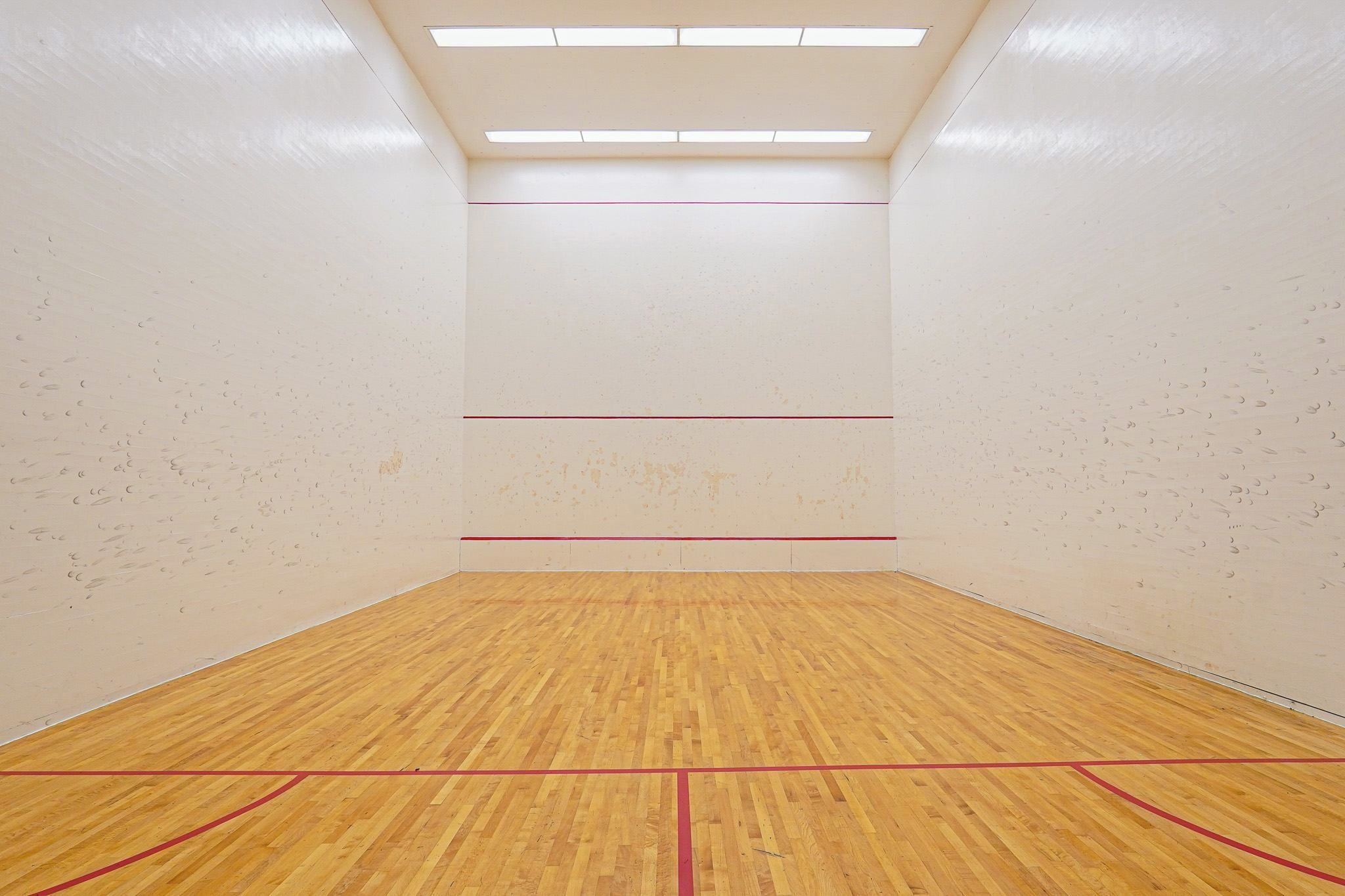 Un court de squash doté d’un plancher en bois et de murs blancs.
