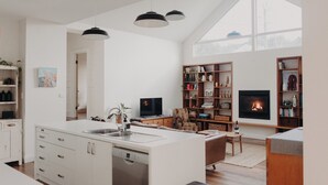 Uma cozinha moderna com ilha central, área de refeições com mesa e cadeiras, lareira e uma grande janela que oferece iluminação natural.