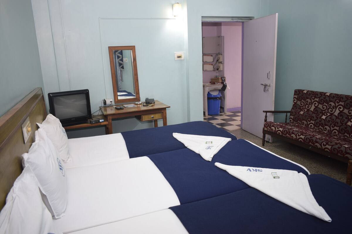 A hotel room with two beds, a desk with a computer, a chair, and a bathroom visible through an open door.