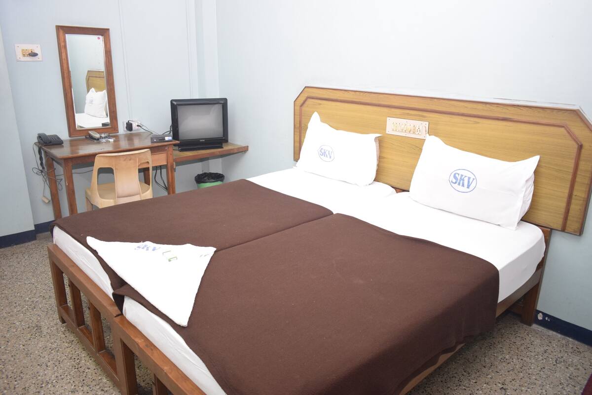 A hotel room with a double bed, a desk with a computer, a chair, and a mirror.