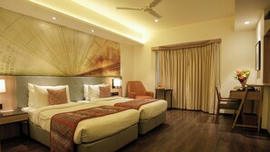 A hotel room with a large bed, a desk, a chair, and a ceiling fan. - Grand Sarovar Portico (Latur)