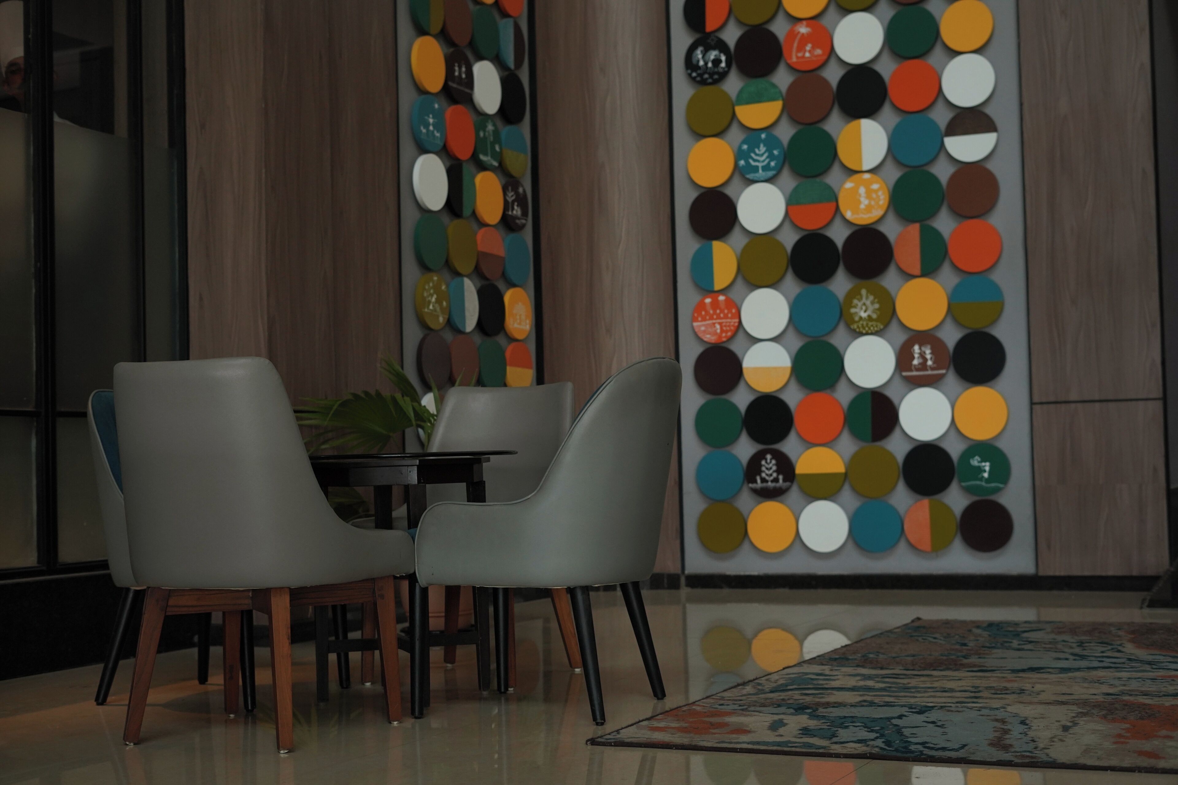 A modern interior with two grey chairs, a small round table, and a colorful wall decoration.
