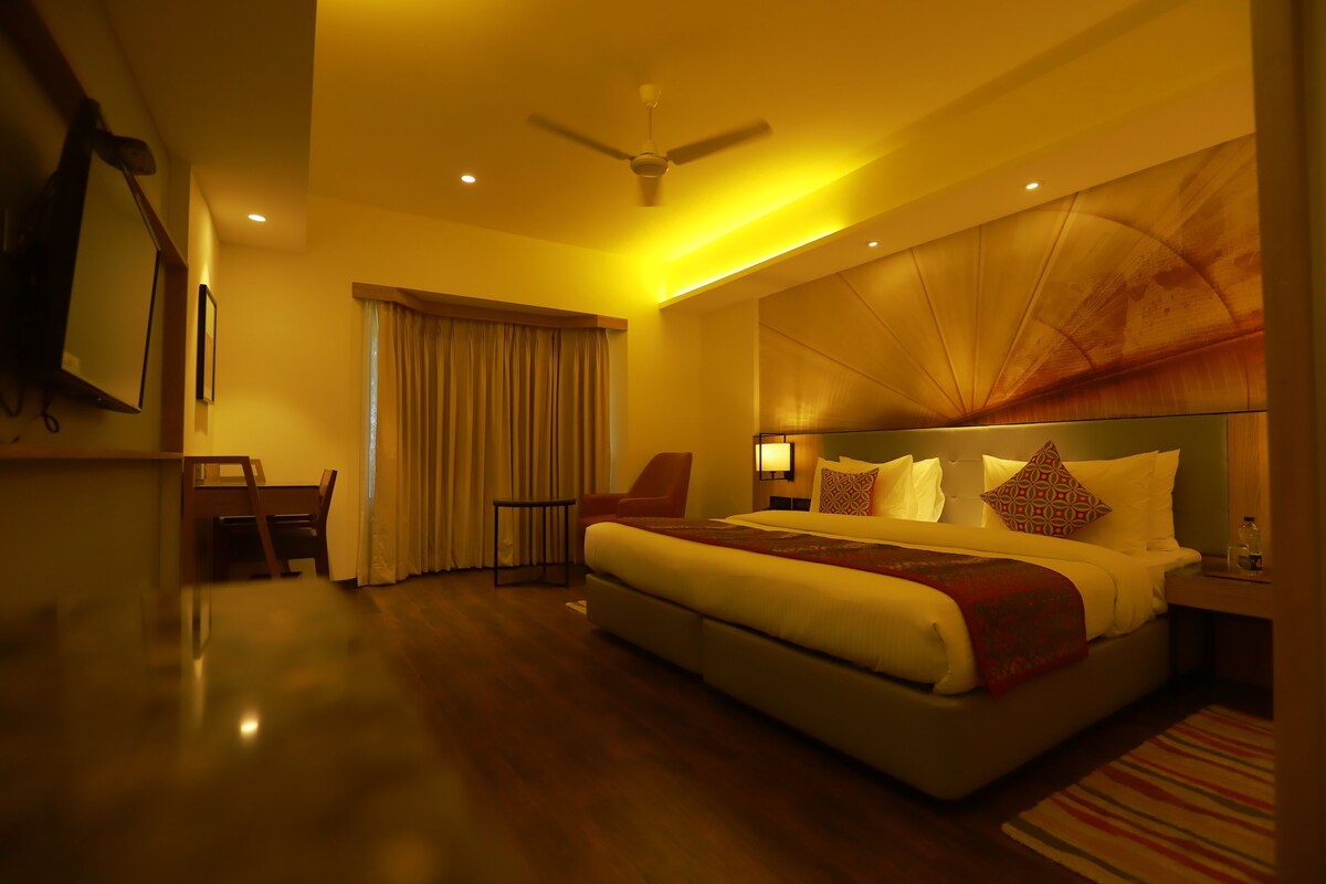 A hotel room with a large bed, a desk, a chair, a ceiling fan, and a window with curtains.