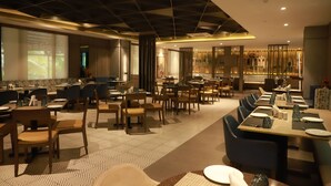 A modern restaurant with a long communal dining area, individual booths, and a bar. - Grand Sarovar Portico (Latur)